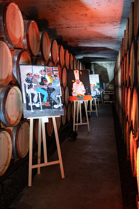 Reportage photo vernissage art dans domaine viticole. Peinture sur chevalet au milieu des tonneaux de vin. Photographie créative Drôme Ardèche. Lumière naturelle.